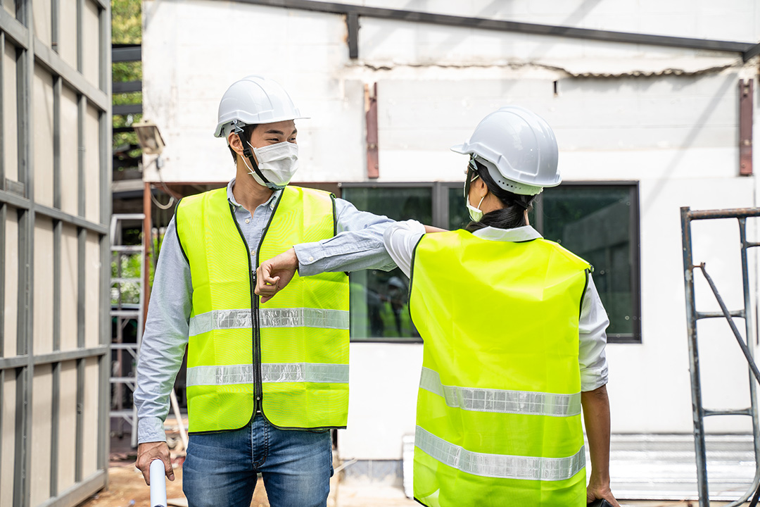 Article Banner Image - A photo of two co-workers greeting each other through the elbow while wearing face masks